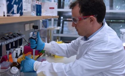 Dr Seth Cheetham, Deputy Director of AIBN’s BASE facility. A man in a white lab coat, goggles and gloves in profile, working at a laboratory bench.